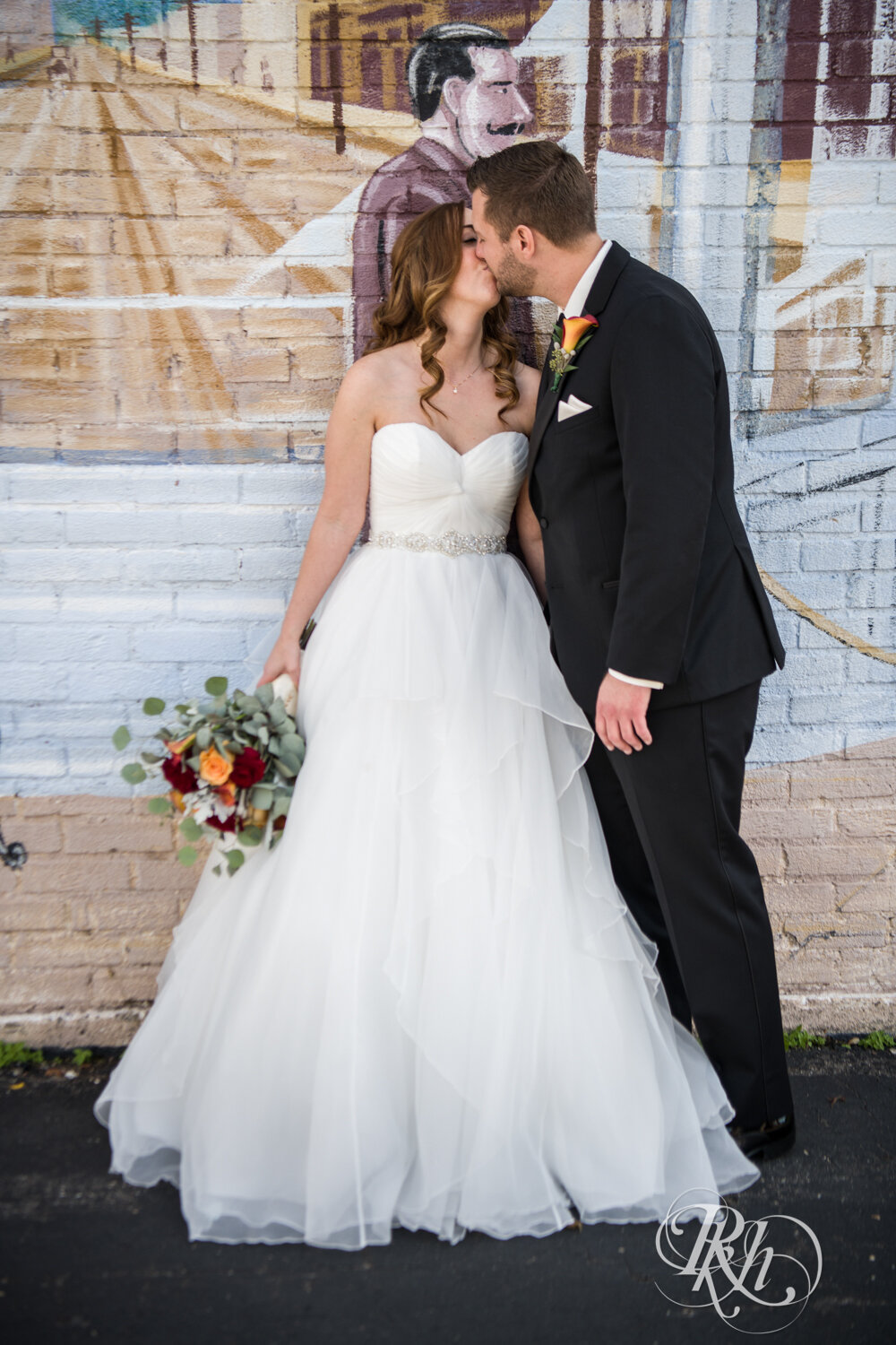 Bride and groom kissing in front of mural in Otsego, Minnesota on sunny wedding day.