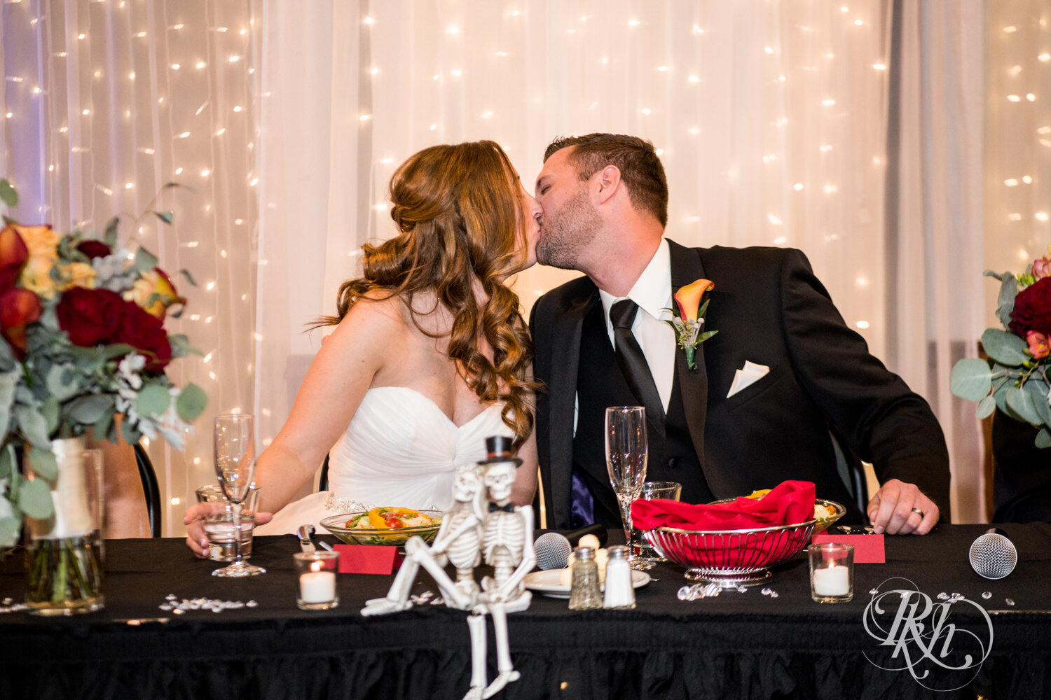 Bride and groom kiss during speeches at wedding reception at Rockwoods in Otsego, Minnesota.