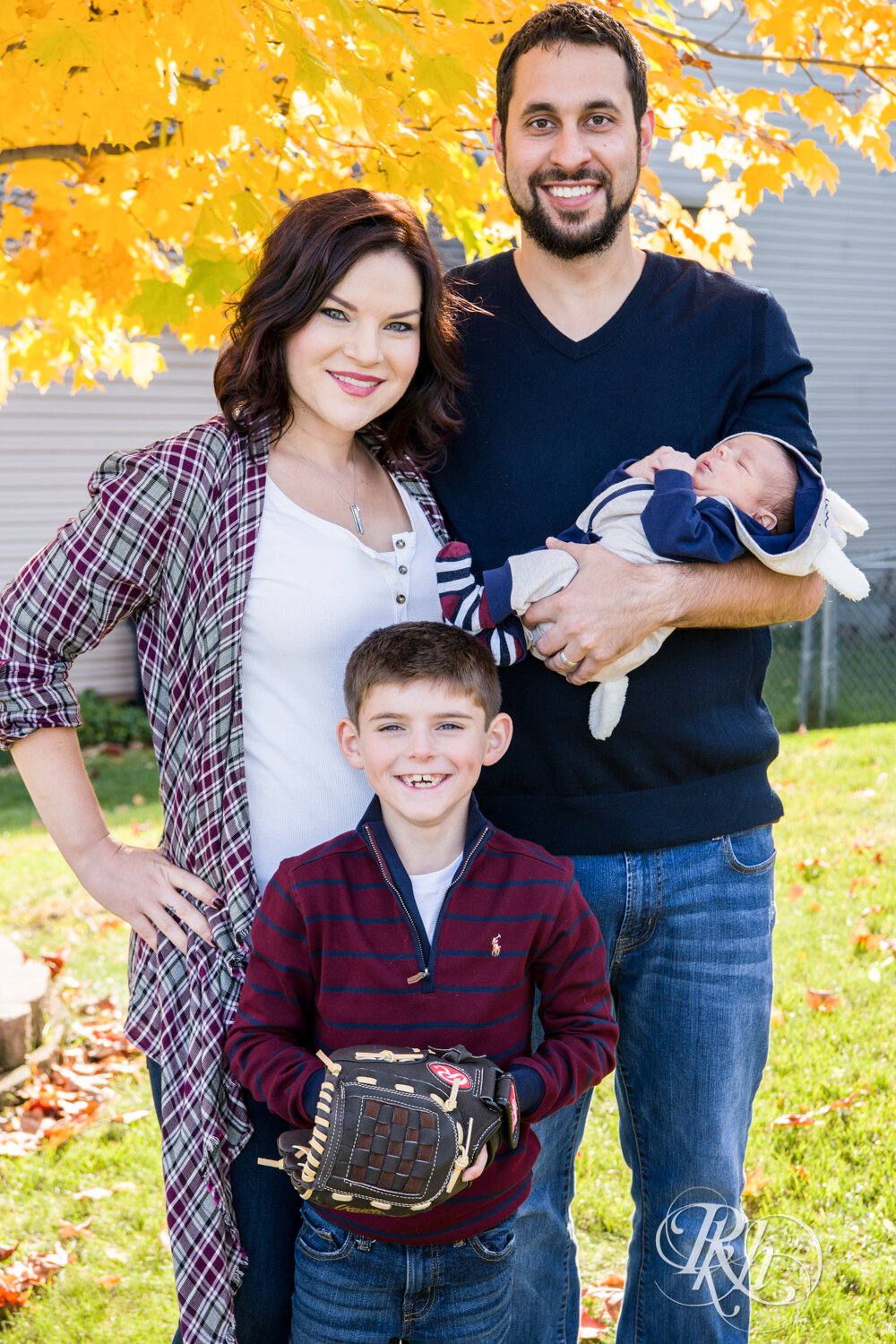 Mom, dad, son and baby smiling in yard with fall colors in Minnesota.