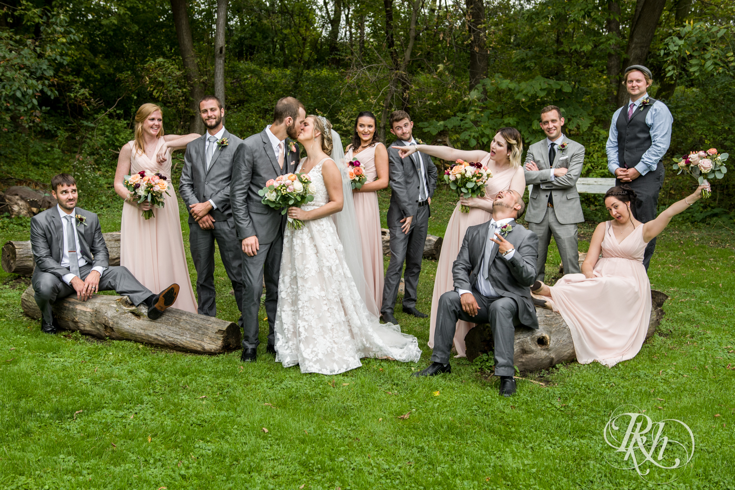 Wedding party in pink dresses and grey suits smile in the rain at Camrose Hill in Stillwater, Minnesota.