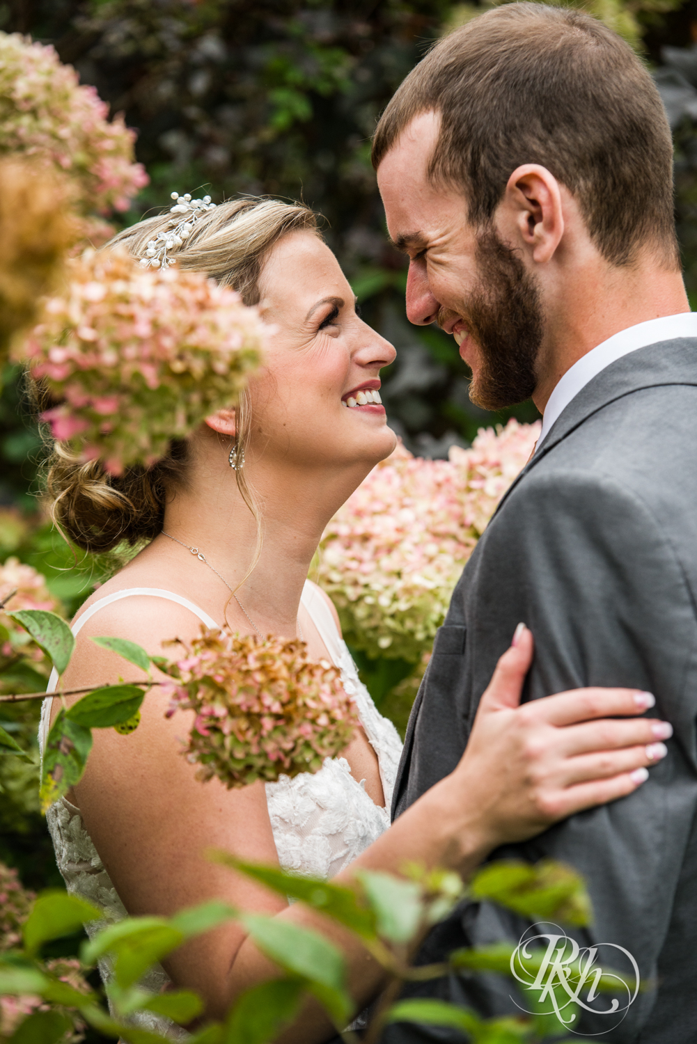 Bride and groom smile in between flowers on rainy day at Camrose Hill in Stillwater, Minnesota.