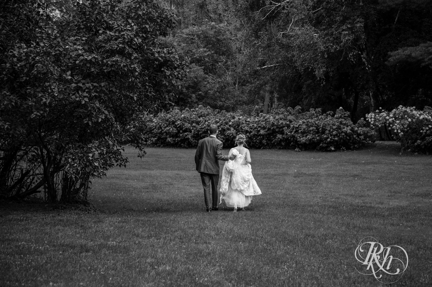 Bride and groom walk across field on rainy day at Camrose Hill in Stillwater, Minnesota.