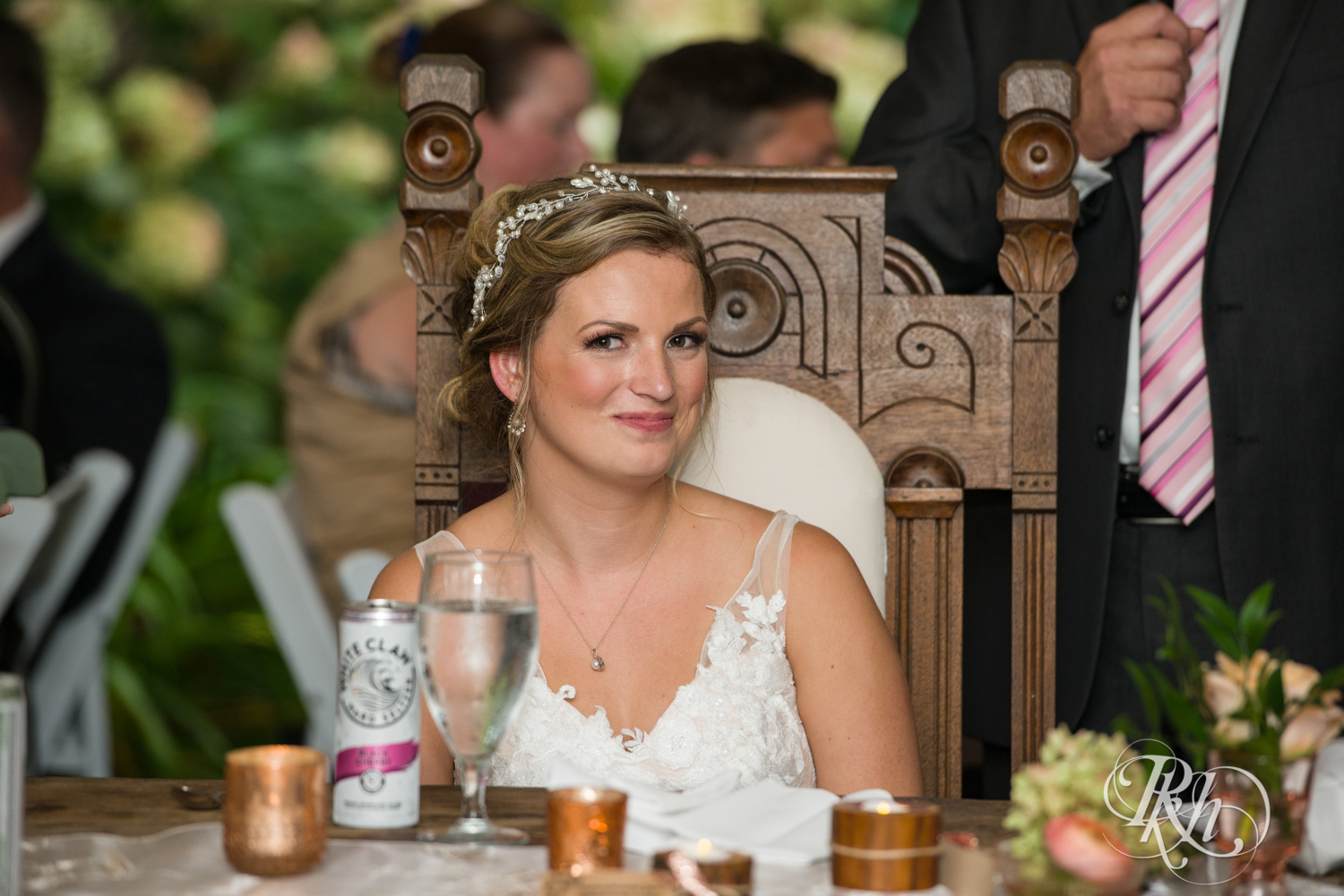 Bride and groom smile during speeches at wedding reception at Camrose Hill in Stillwater, Minnesota.