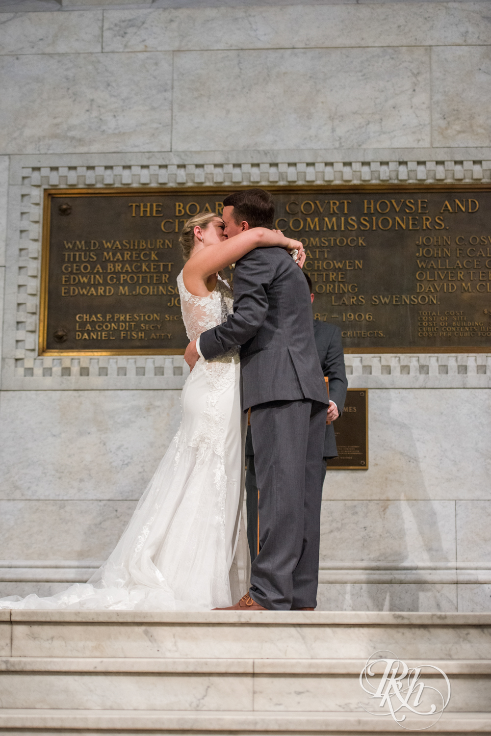 Bride and groom kiss during ceremony on stairs at Minneapolis City Hall in Minneapolis, Minnesota.