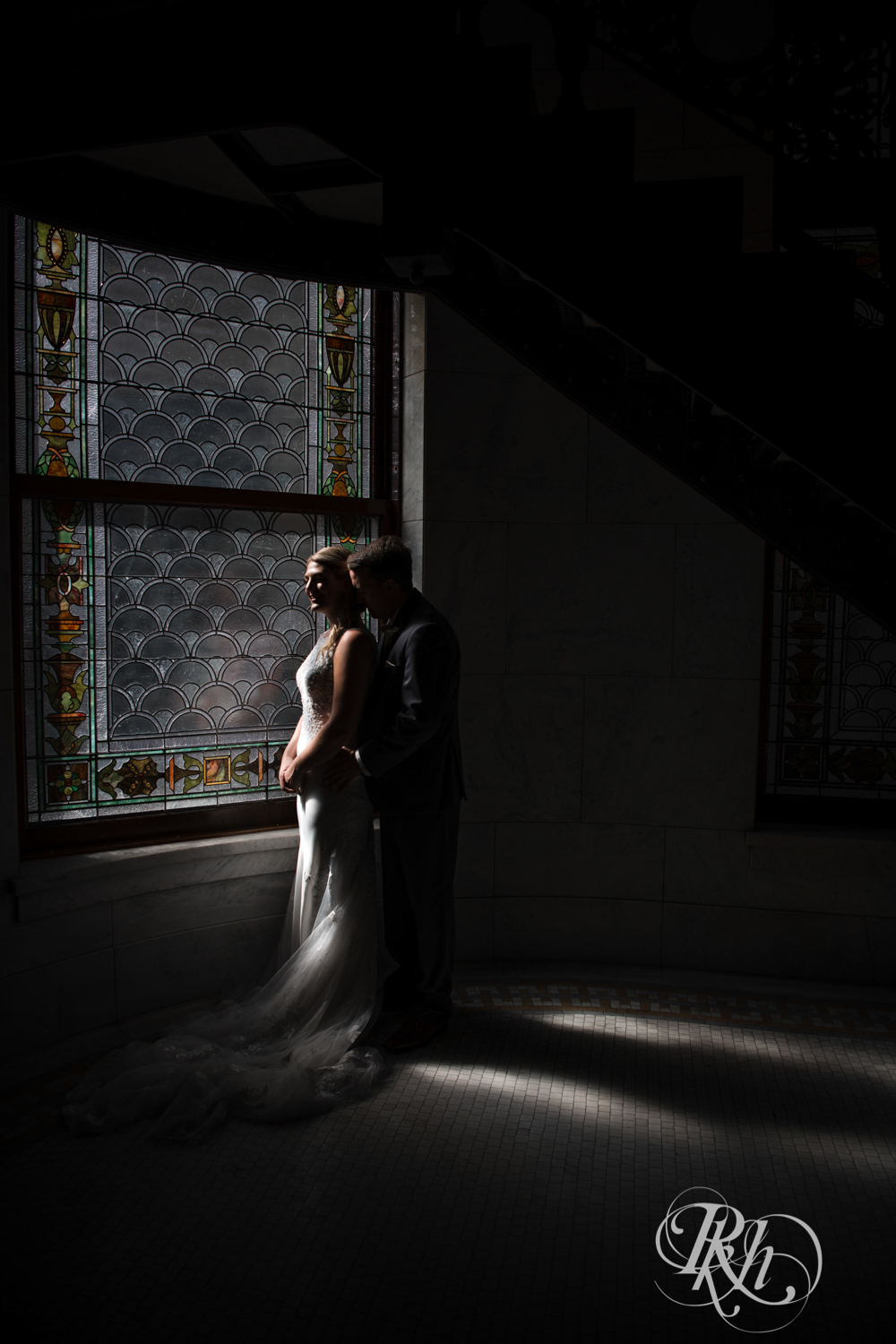 Bride and groom stand in front of window in Minneapolis City Hall in Minneapolis, Minnesota.