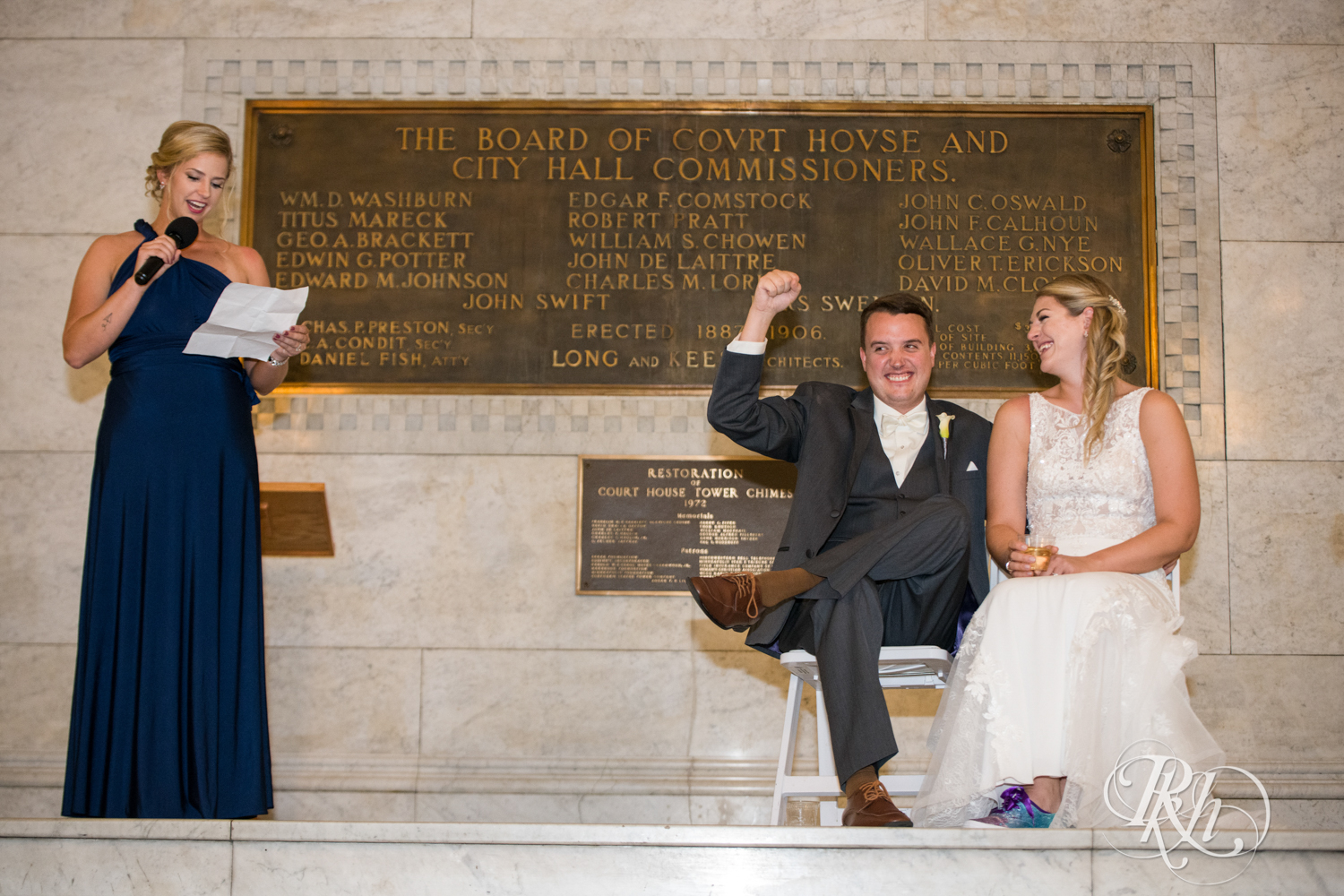 Bride and groom smile during speeches at wedding reception in Minneapolis City Hall in Minneapolis, Minnesota.