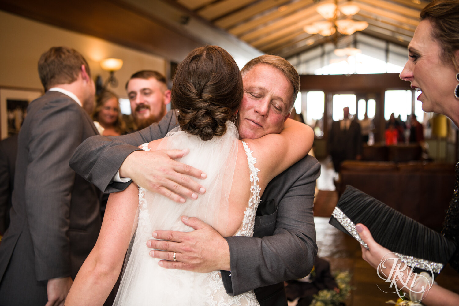 Dad hugs bride after wedding ceremony on rainy day at The Wilds Golf Club in Prior Lake, Minnesota.