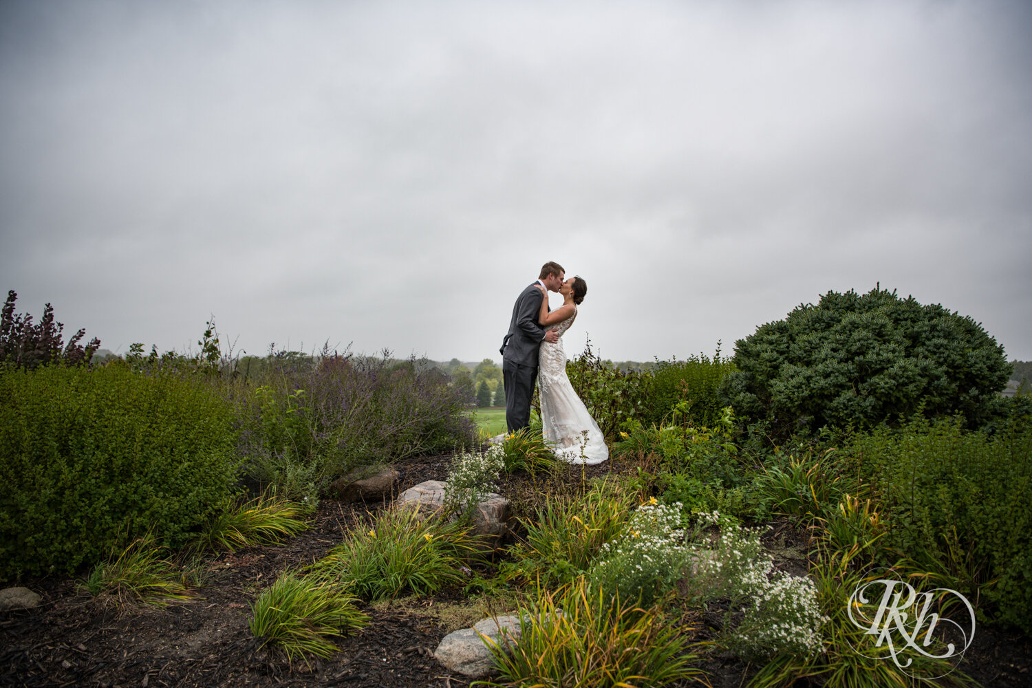 Bride and groom kiss under storm clouds on rainy day