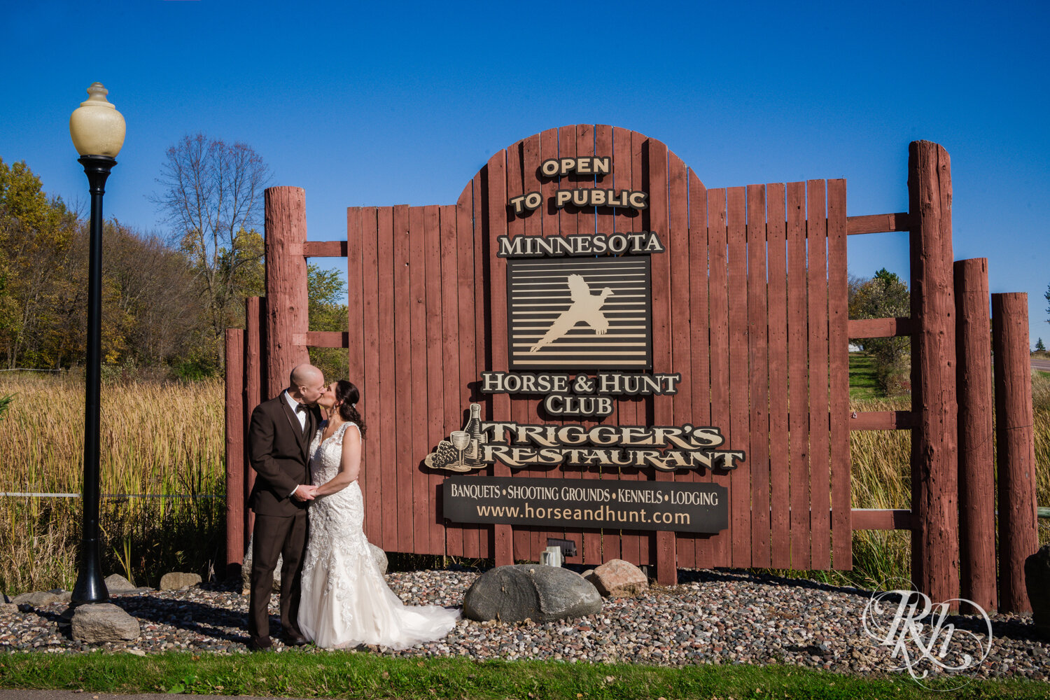 Bride and groom kiss in front of the sign at Minnesota Horse and Hunt Club in Prior Lake, Minnesota.