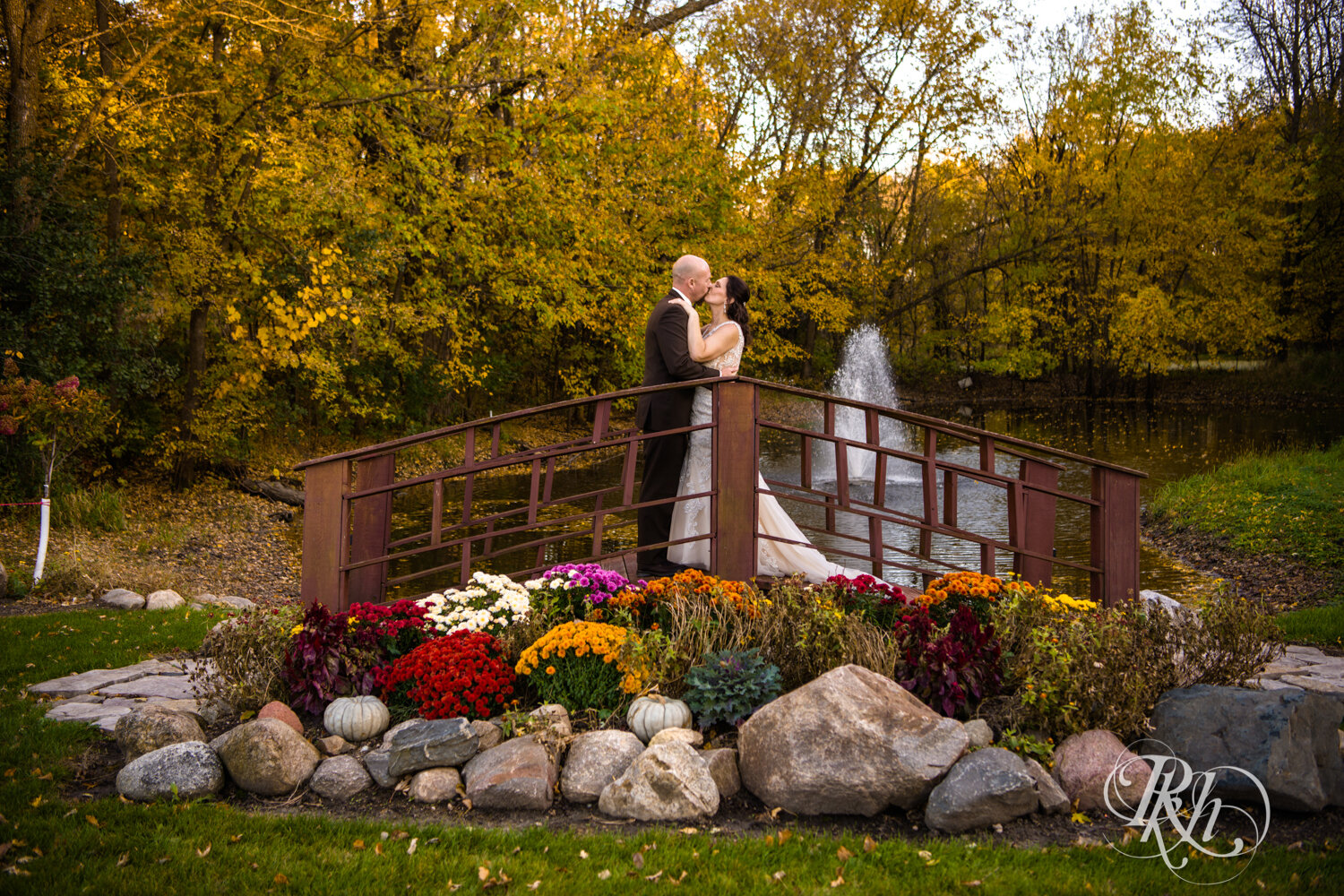 Bride and groom kiss on bridge with fall colors at sunset at Minnesota Horse and Hunt Club in Prior Lake, Minnesota.