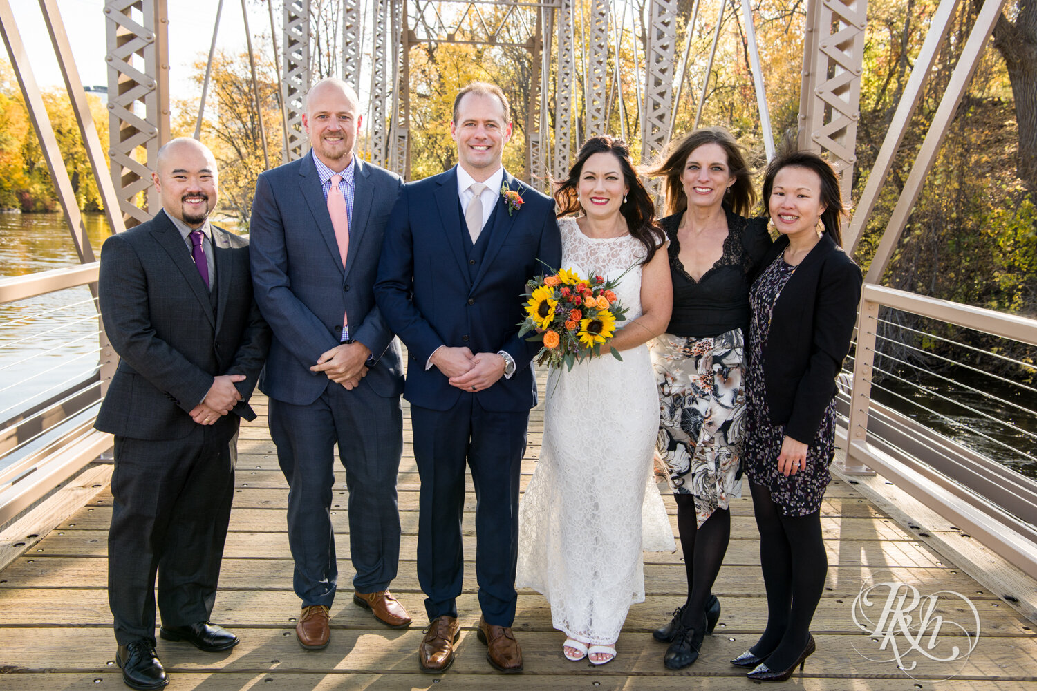 Bride and groom smile with wedding party on bridge on Boom Island in Minneapolis, Minnesota.