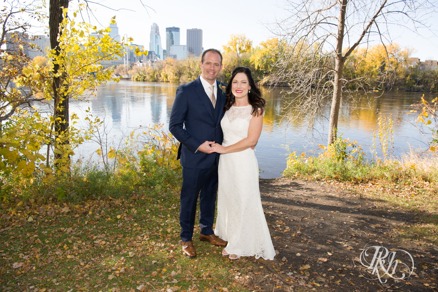 Bride and groom smile in front of river on Boom Island in Minneapolis, Minnesota.