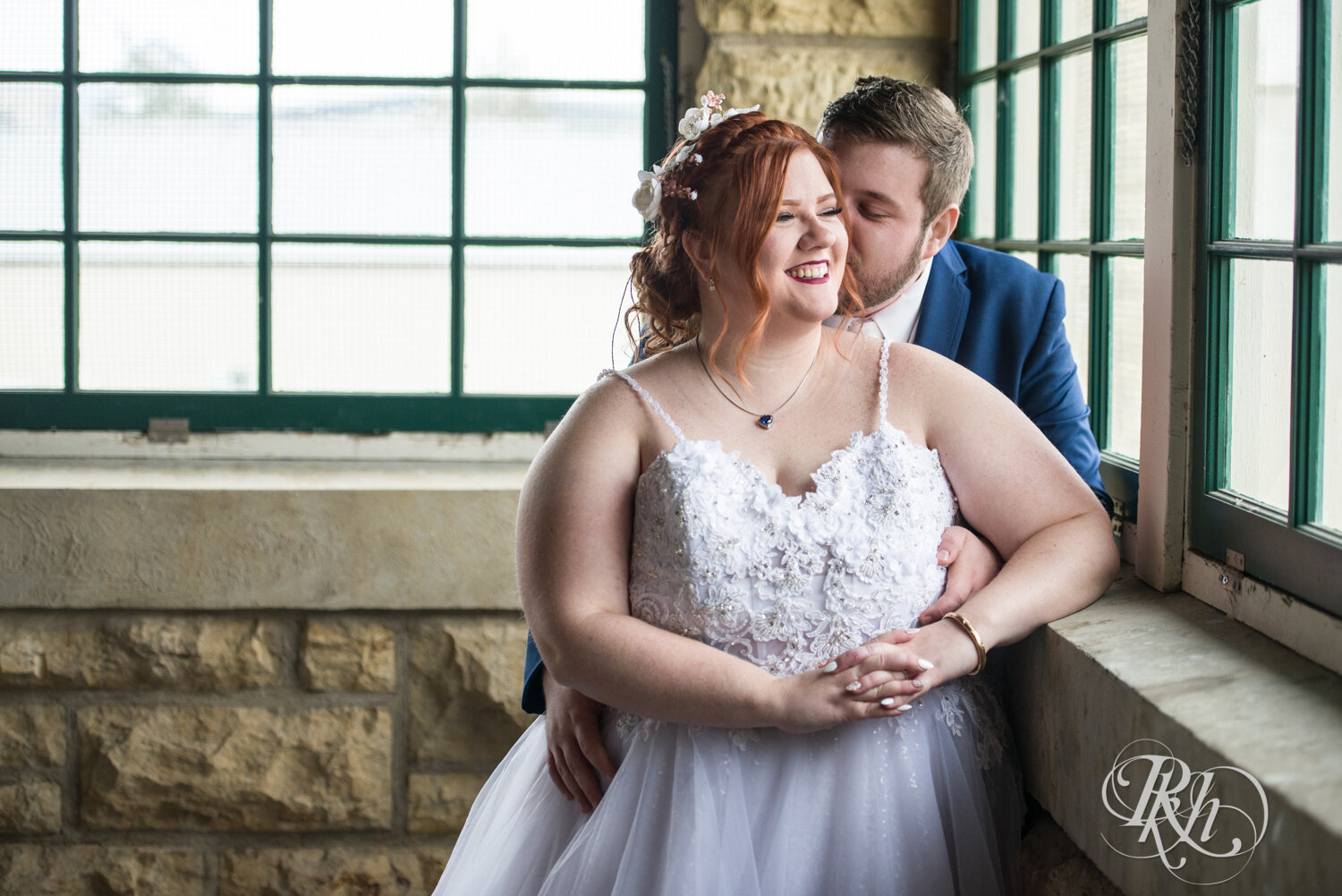 Plus size bride and groom kiss by window at wedding at Olmsted County Fairgrounds in Rochester, Minnesota.