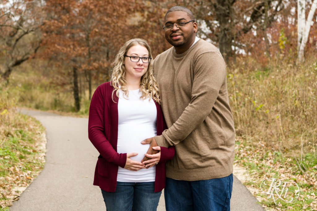 Black man and white woman biracial couple hold pregnant belly in Lebanon Hills Regional Park in Eagan, Minnesota. 