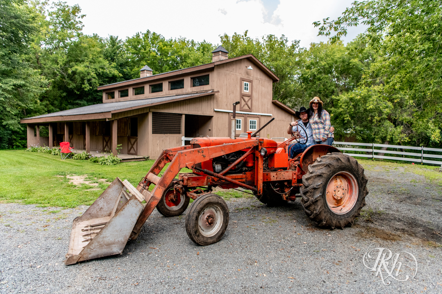 Lebanese woman and man in cowboy hats smile on tractor at their horse farm in Chisago City, Minnesota.