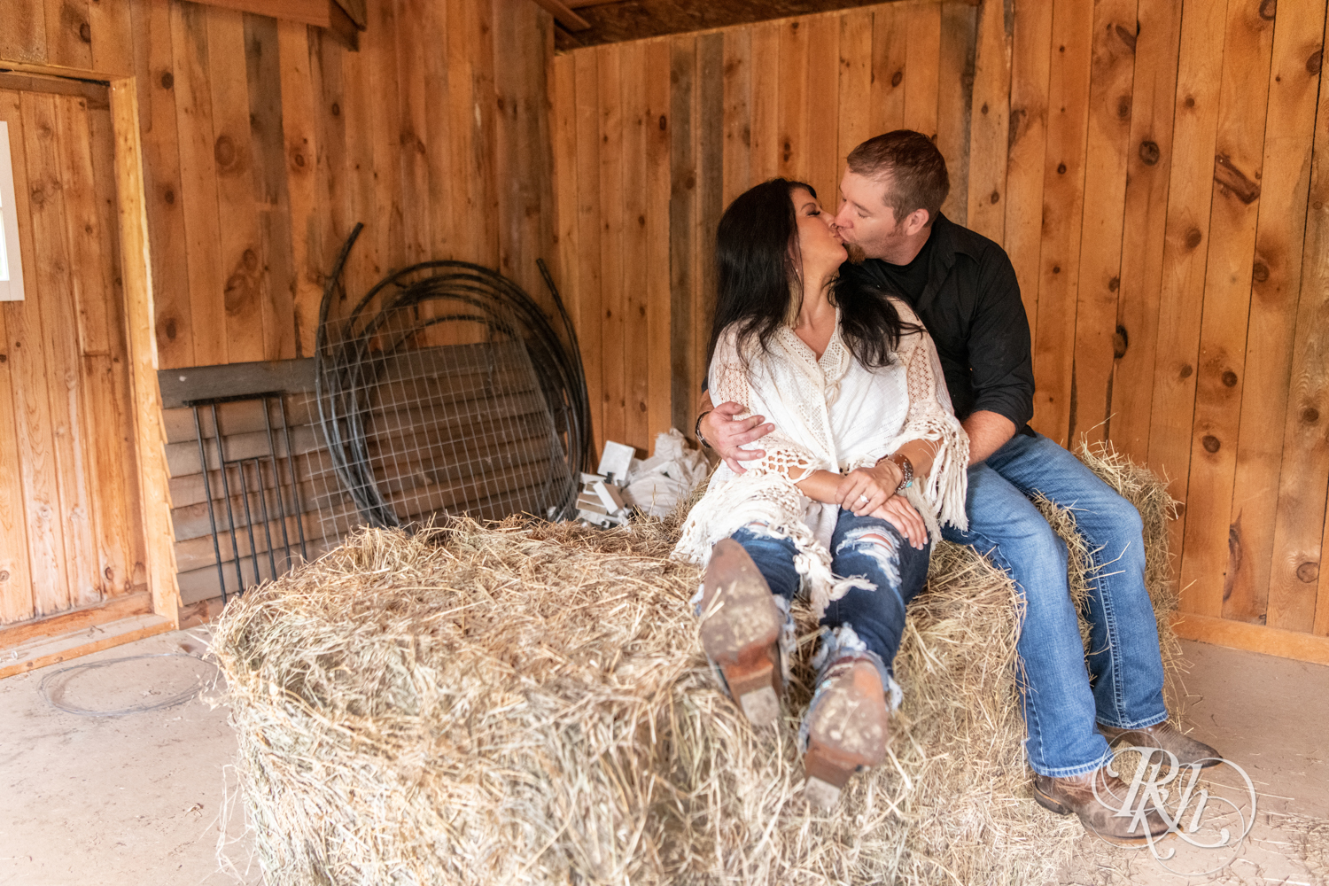 Lebanese woman and man kiss in hay bale at their horse farm in Chisago City, Minnesota.