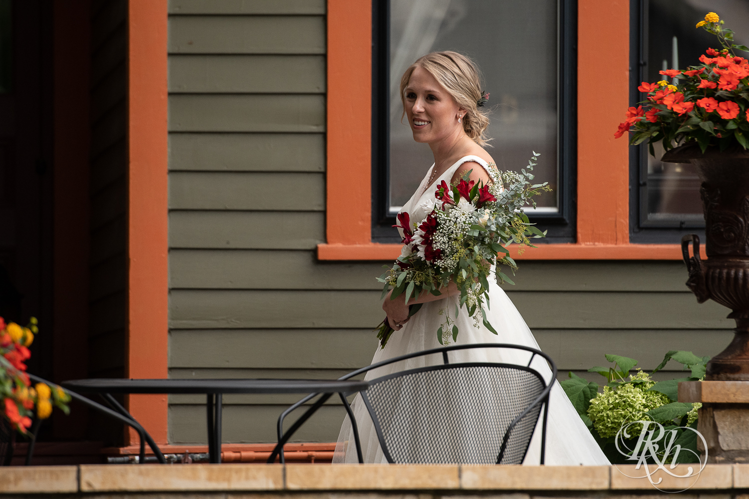 Bride walking down the aisle at the William Sauntry Mansion in Stillwater, Minnesota in the fall holding red and white flowers.