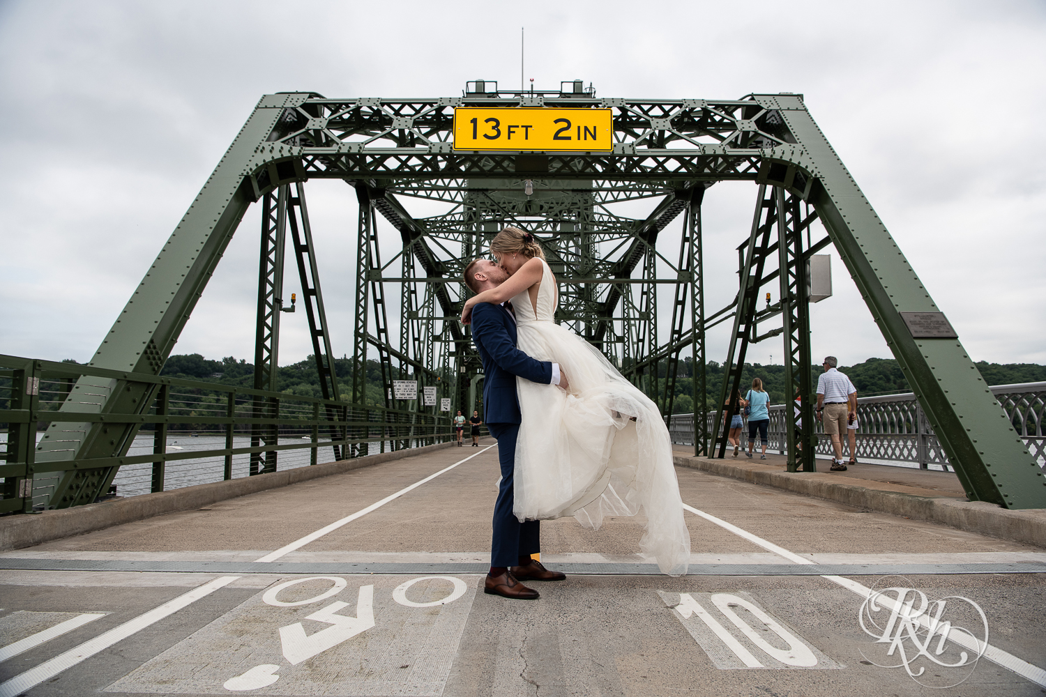 groom lifting bride up in front of bridge