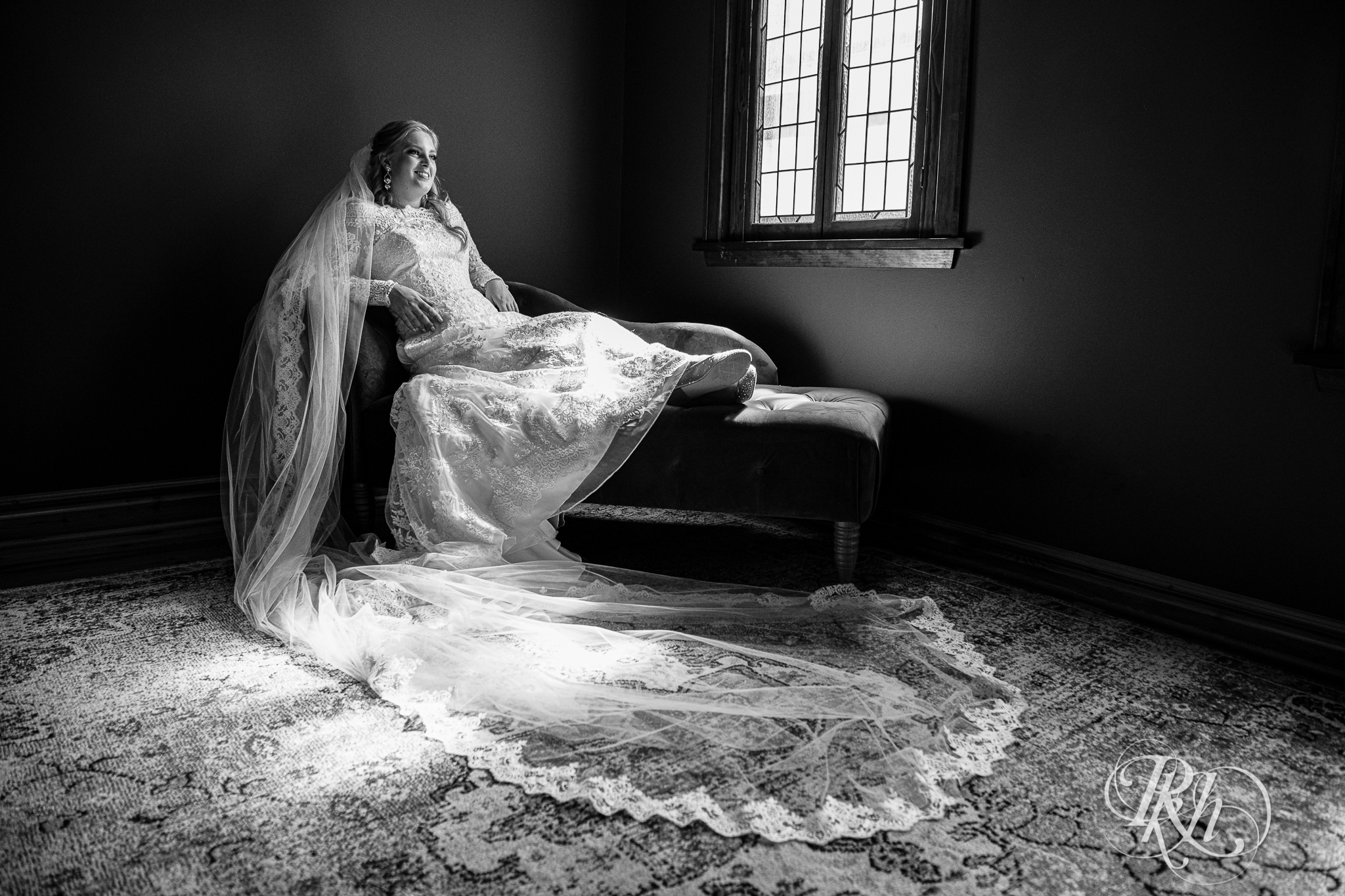 Bride sitting on couch in long sleeve wedding dress and cathedral veil at Weddings at the Broz in New Prague, Minnesota.