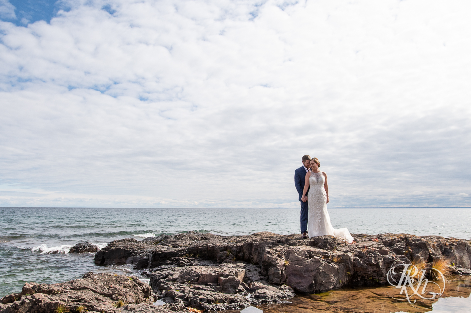 Bride and groom smile on rock in front of Lake Superior at Superior Shores Resort in Two Harbors, Minnesota.