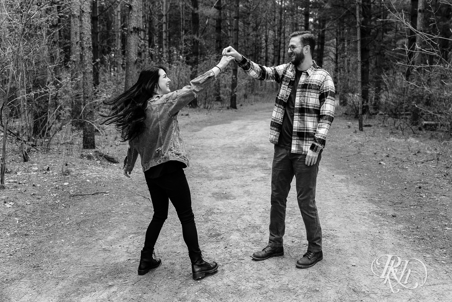 Man and woman in denim and flannel dance between trees at Lebanon Hills Regional Park in Eagan, Minnesota. 