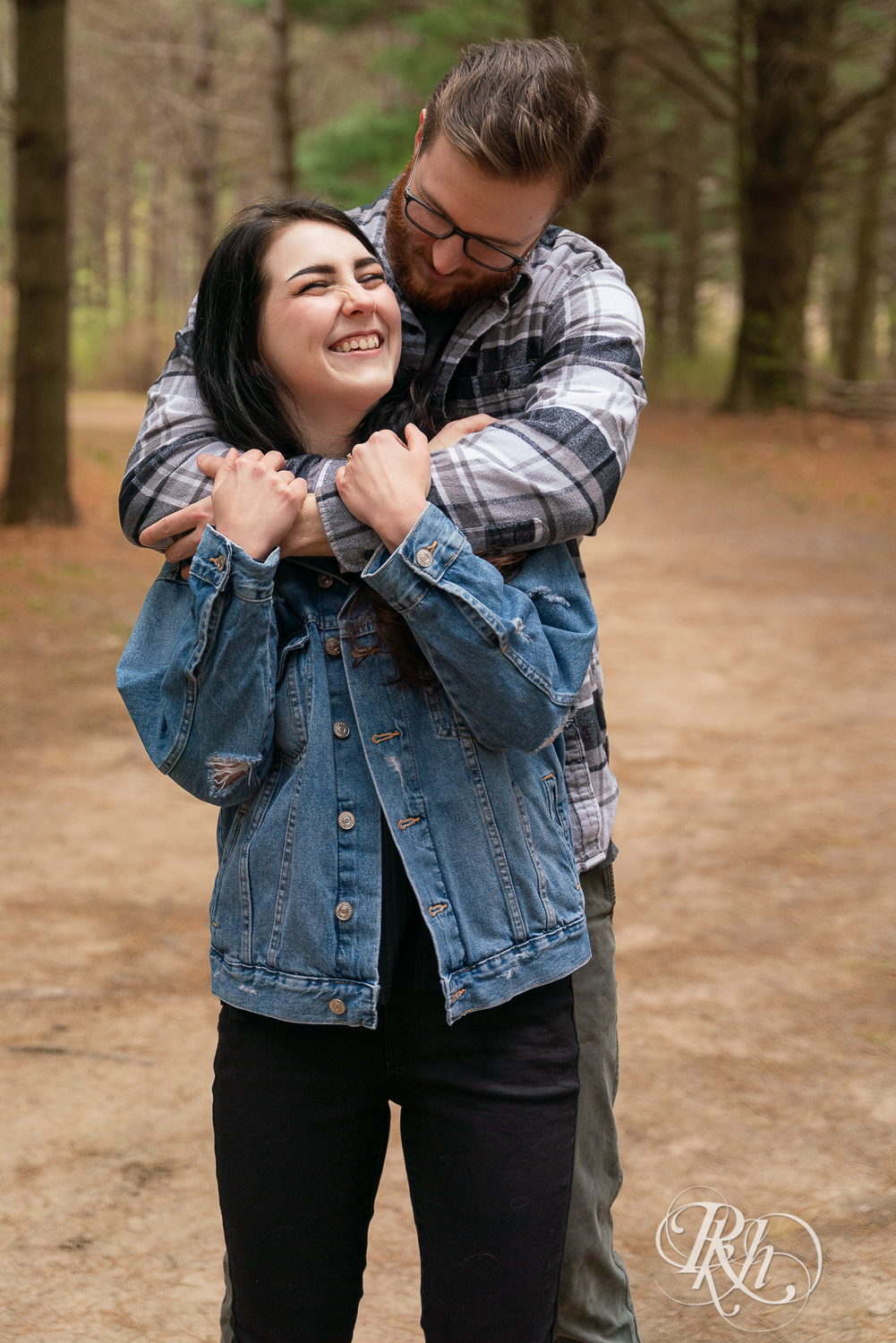 Man and woman in denim and flannel snuggle between trees at Lebanon Hills Regional Park in Eagan, Minnesota. 