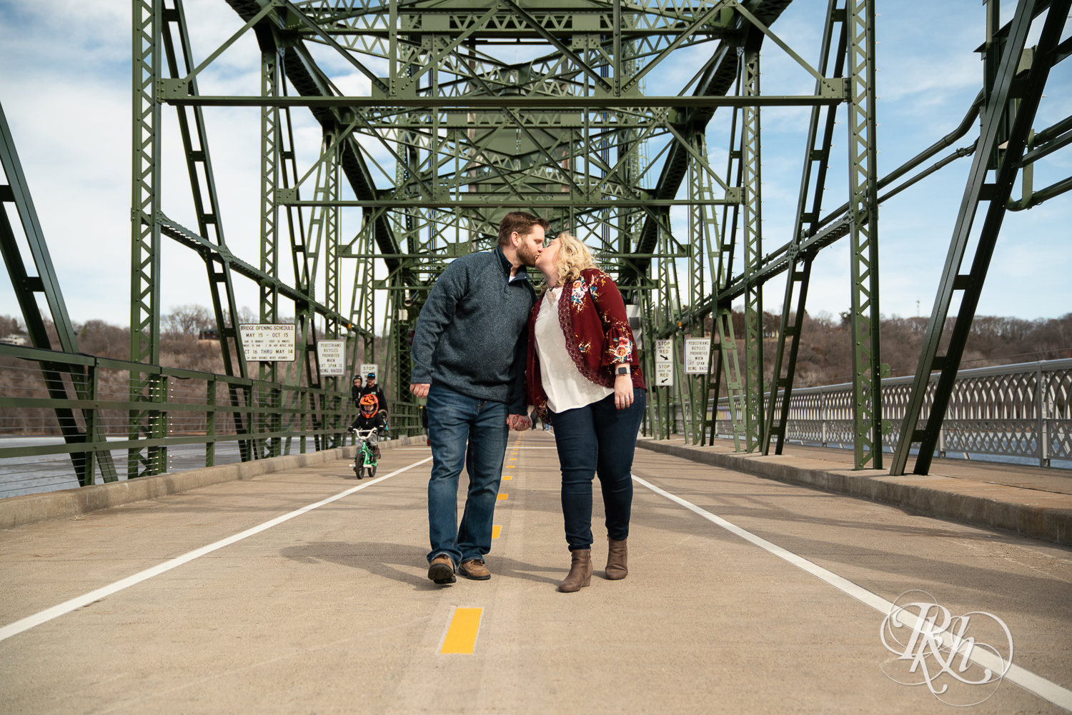 Blond woman and bearded man kiss on bridge over river in Stillwater, Minnesota.