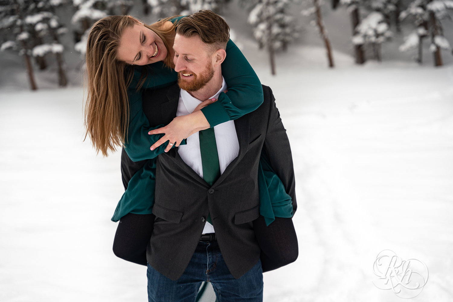 Man in suit and woman in green dress do piggy back ride in snow on Dream Lake in Rocky Mountain National Park, Colorado.