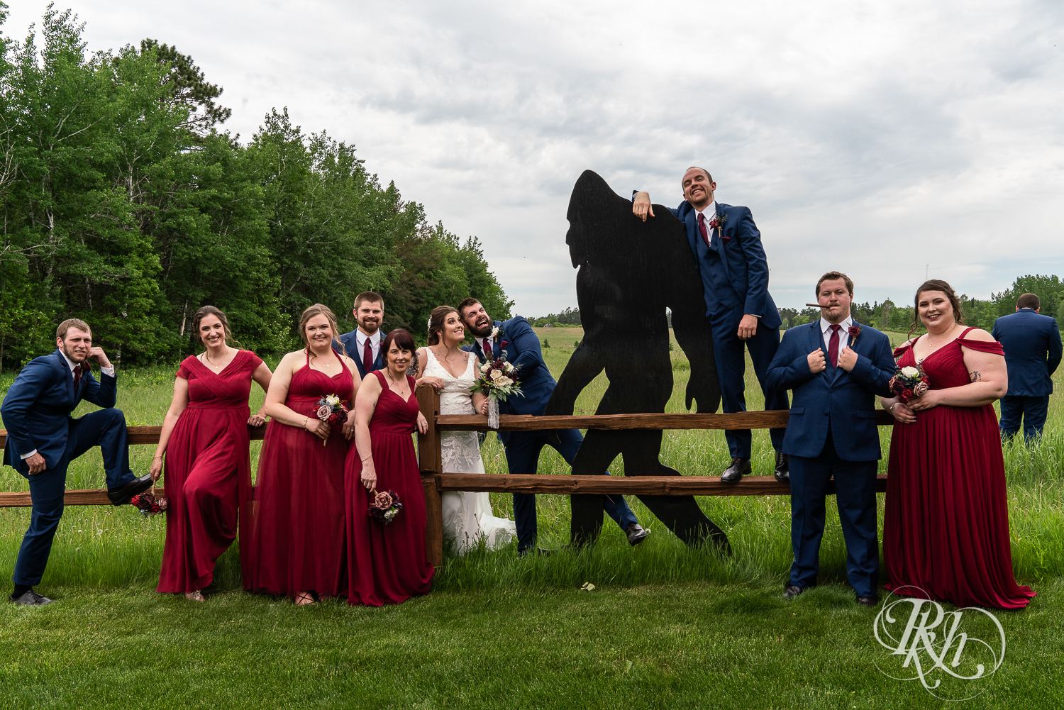 Wedding party in red dresses and blue suits pose with Bigfoot at Pine Peaks Event Center in Pine River, Minnesota.