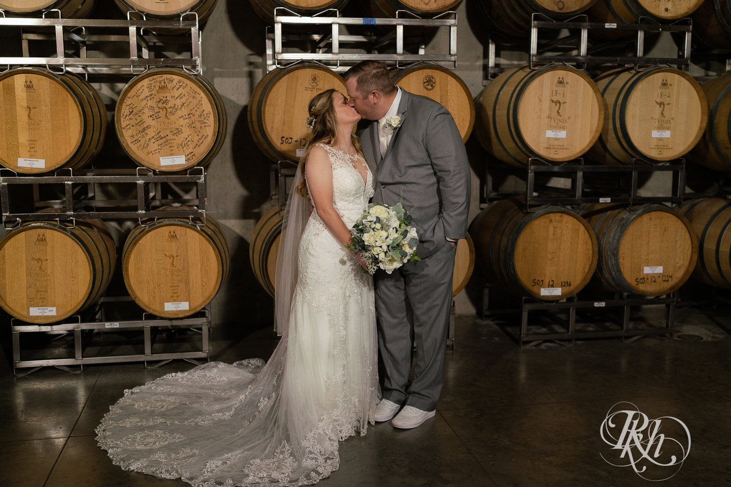 Bride and groom kissing in front of wine barrels at 7 Vines Vineyard in Dellwood, Minnesota.