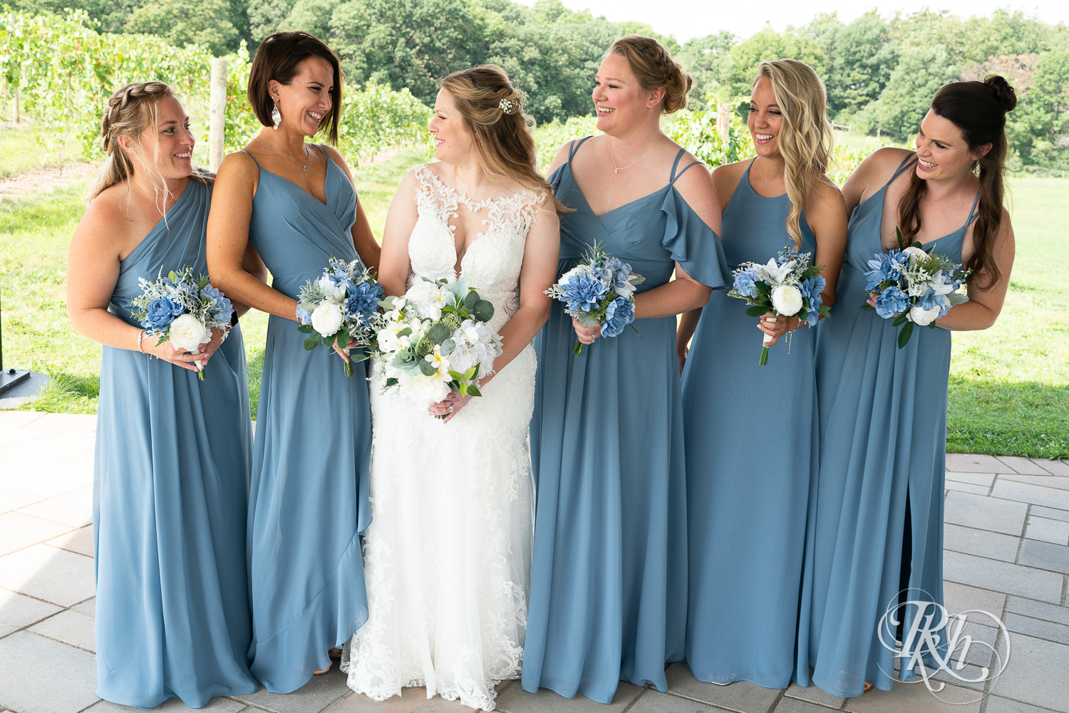 Wedding party in blue dresses smiling at 7 Vines Vineyard in Dellwood, Minnesota.