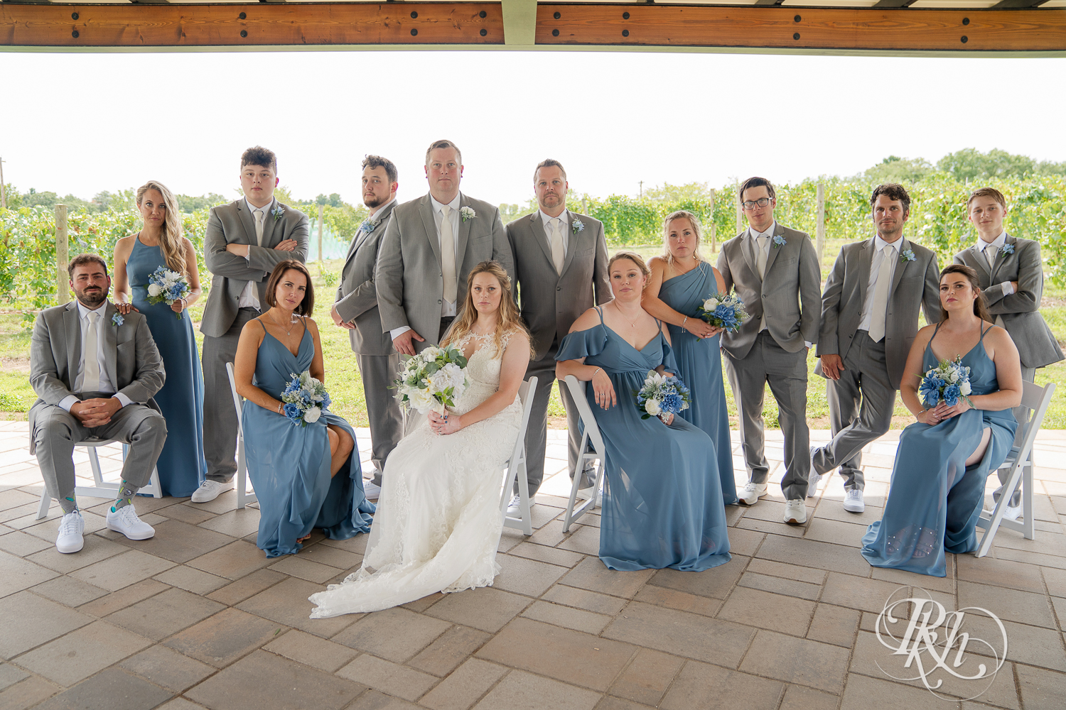 Wedding party in grey suits and blue dresses smiling at 7 Vines Vineyard in Dellwood, Minnesota.