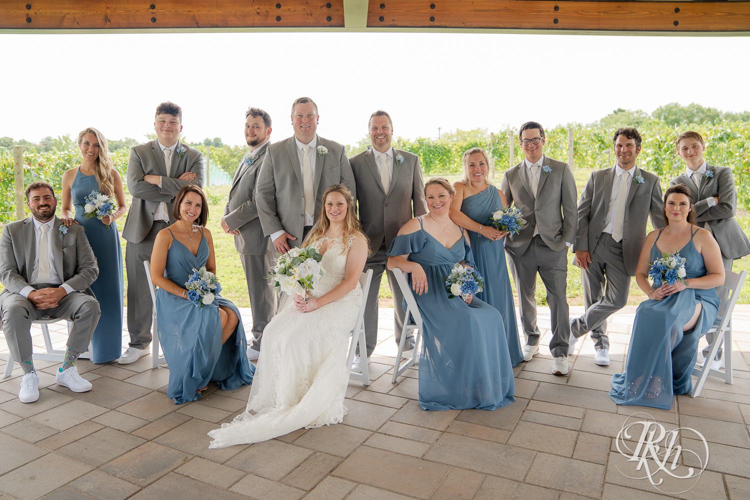 Wedding party in grey suits and blue dresses smiling at 7 Vines Vineyard in Dellwood, Minnesota.