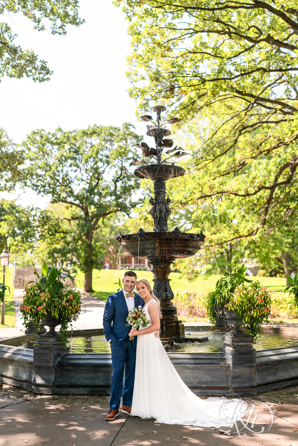 Bride and groom smile and laugh together at Irvine Park in Saint Paul, Minnesota in front of fountain.