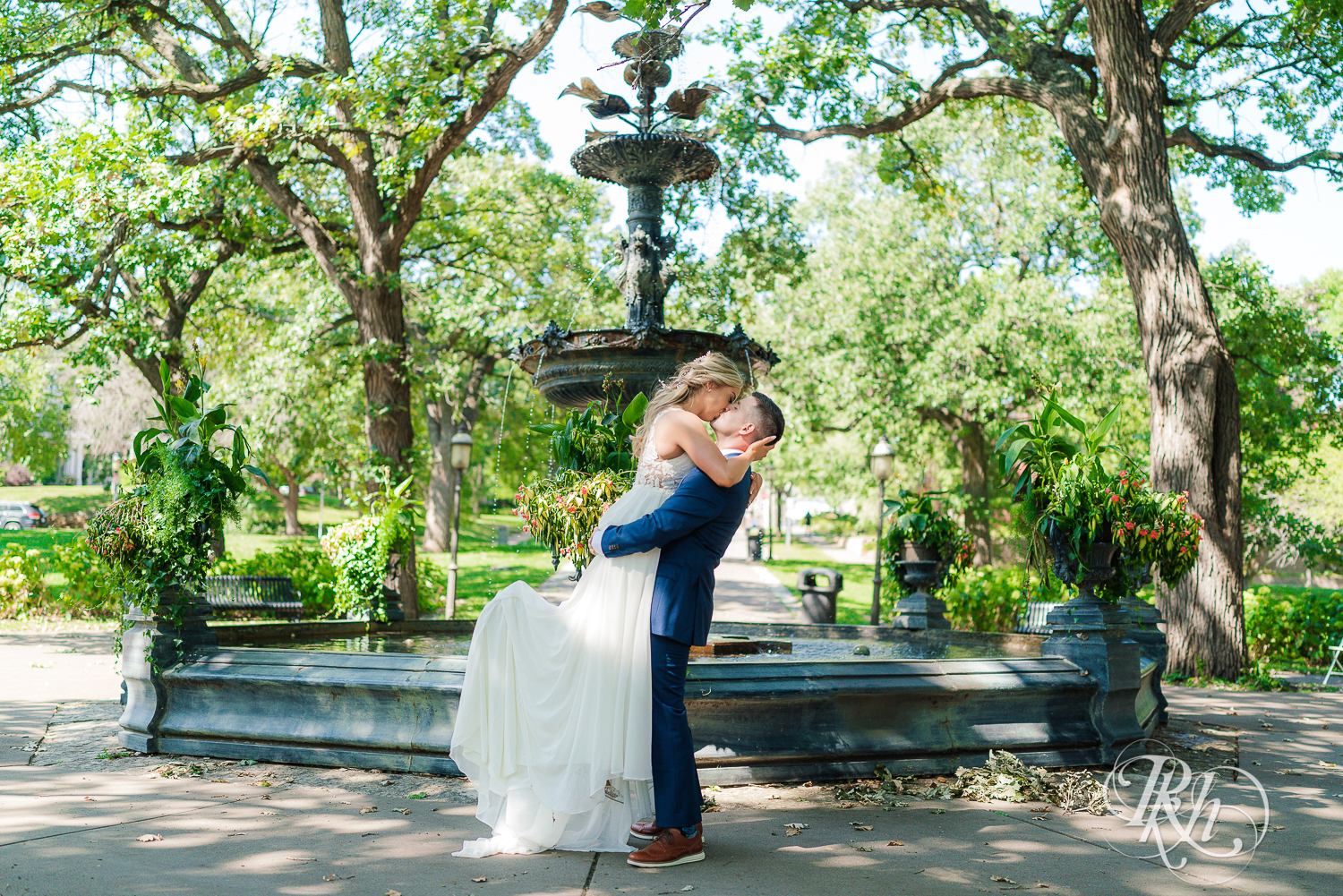 Groom lifts and kisses bride in front of fountain at Irvine Park in Saint Paul, Minnesota.