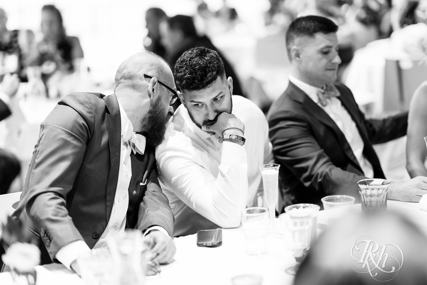 Groomsmen converse during wedding reception at head table at Saint Paul Event Center in Saint Paul, Minnesota.