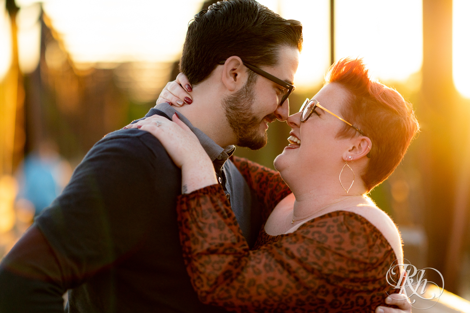 Man and woman in glasses laughing at sunset.