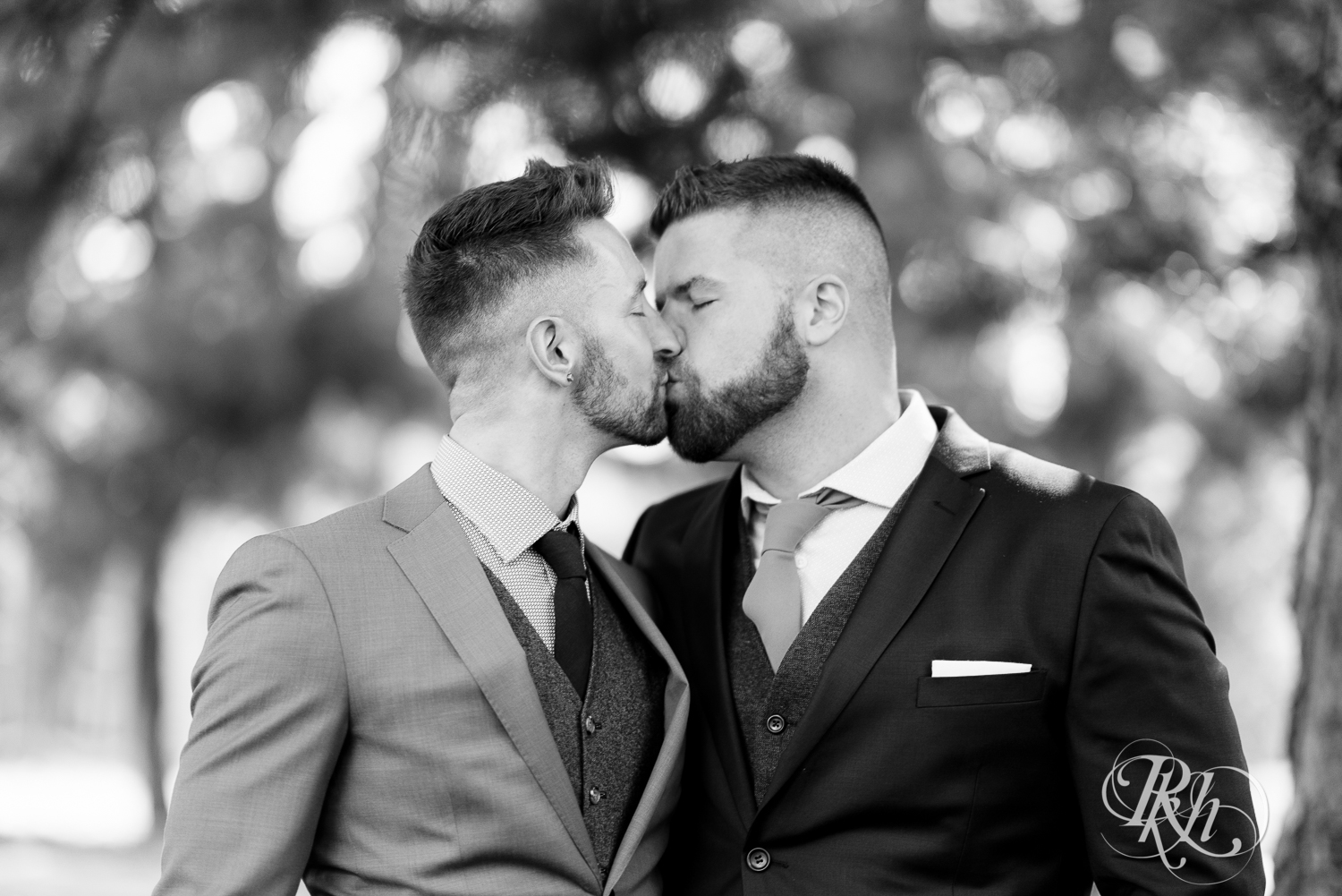 Gay grooms in blue suits kissing on wedding day at Nicollet Island in Minneapolis, Minnesota.