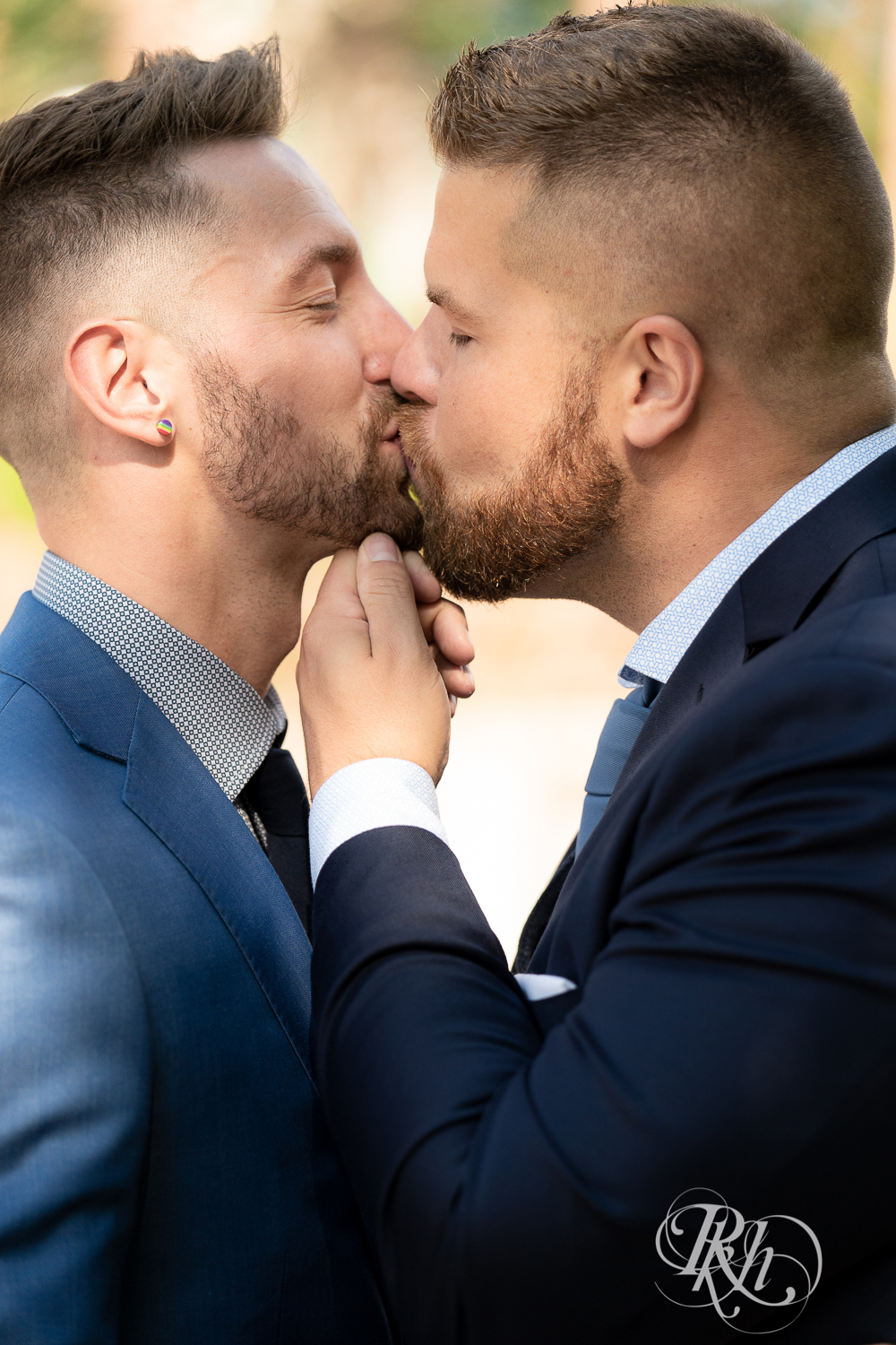 Gay grooms in blue suits kissing on sunny wedding day at Nicollet Island in Minneapolis, Minnesota.