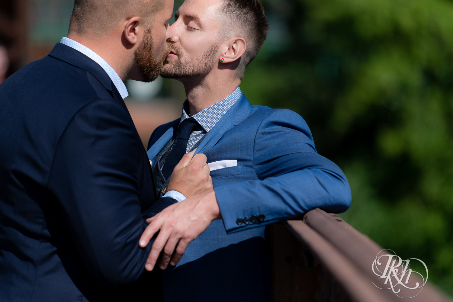 Gay grooms in blue suits kissing on sunny wedding day at Nicollet Island in Minneapolis, Minnesota.