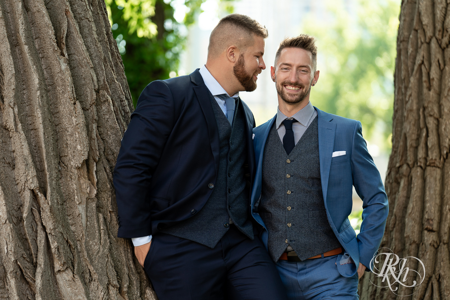 Gay grooms in blue suits smiling on sunny wedding day at Nicollet Island in Minneapolis, Minnesota.