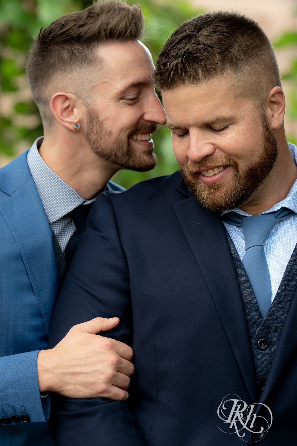 Gay grooms in blue suits smiling on sunny wedding day at Nicollet Island in Minneapolis, Minnesota.