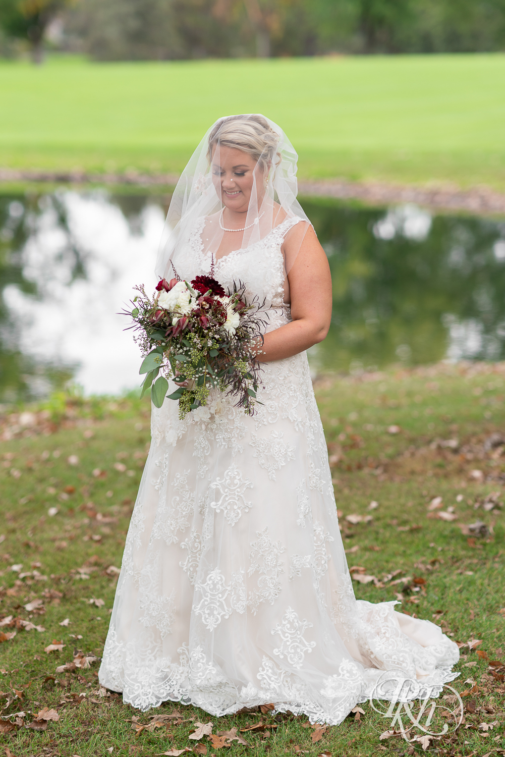Bride under veil holds red and white flowers at Hastings Golf Club in Hastings, Minnesota.