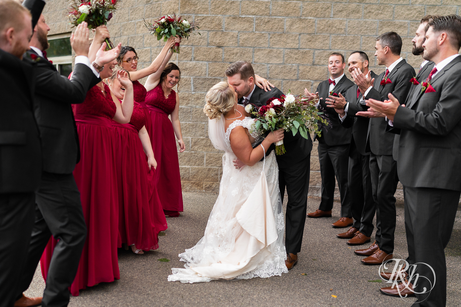 Wedding party in red dresses and gray suits surround kissing couple at Hastings Golf Club in Hastings, Minnesota.