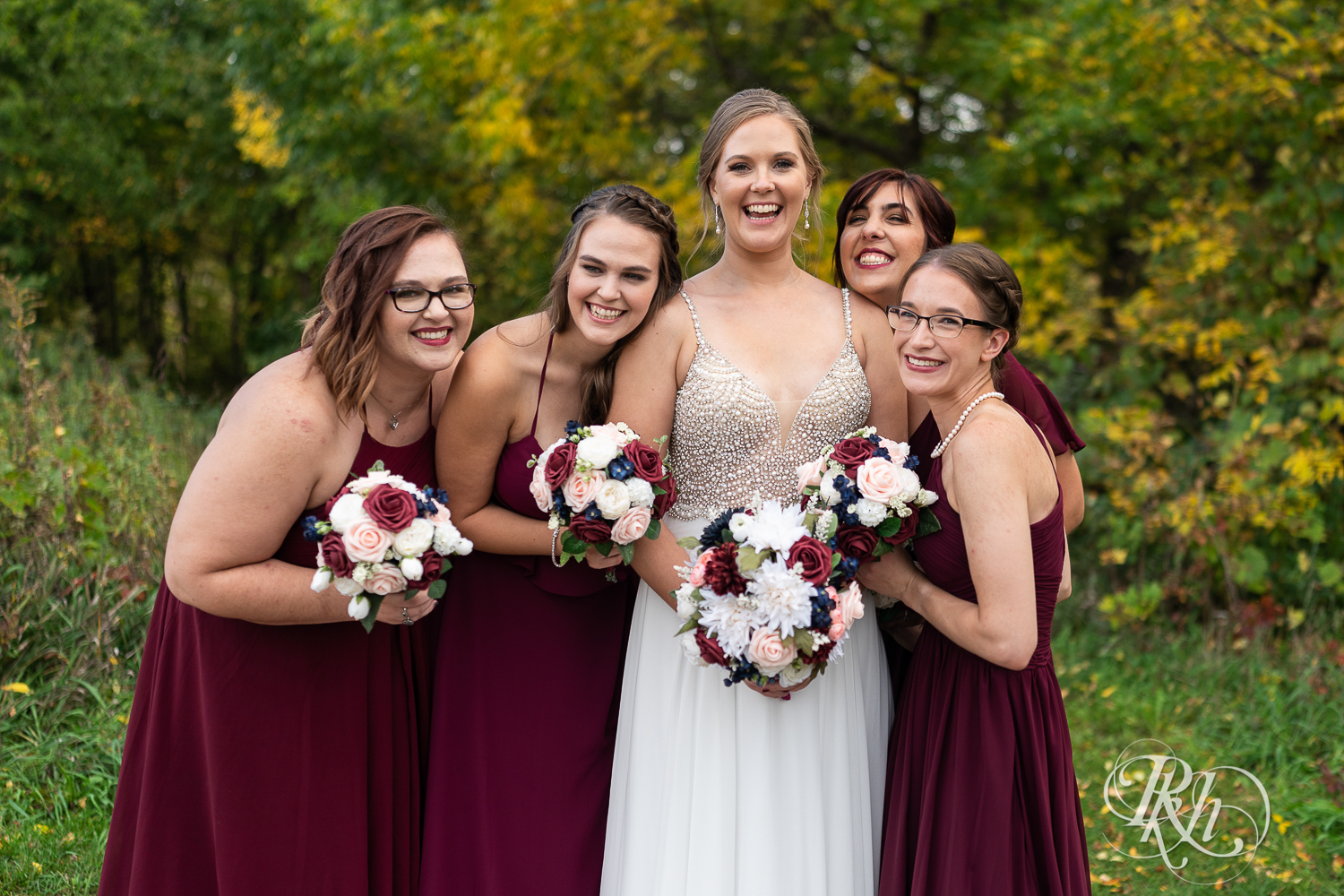 Wedding party smiling in red dresses at Schaar's Bluff in Hastings, Minnesota. 