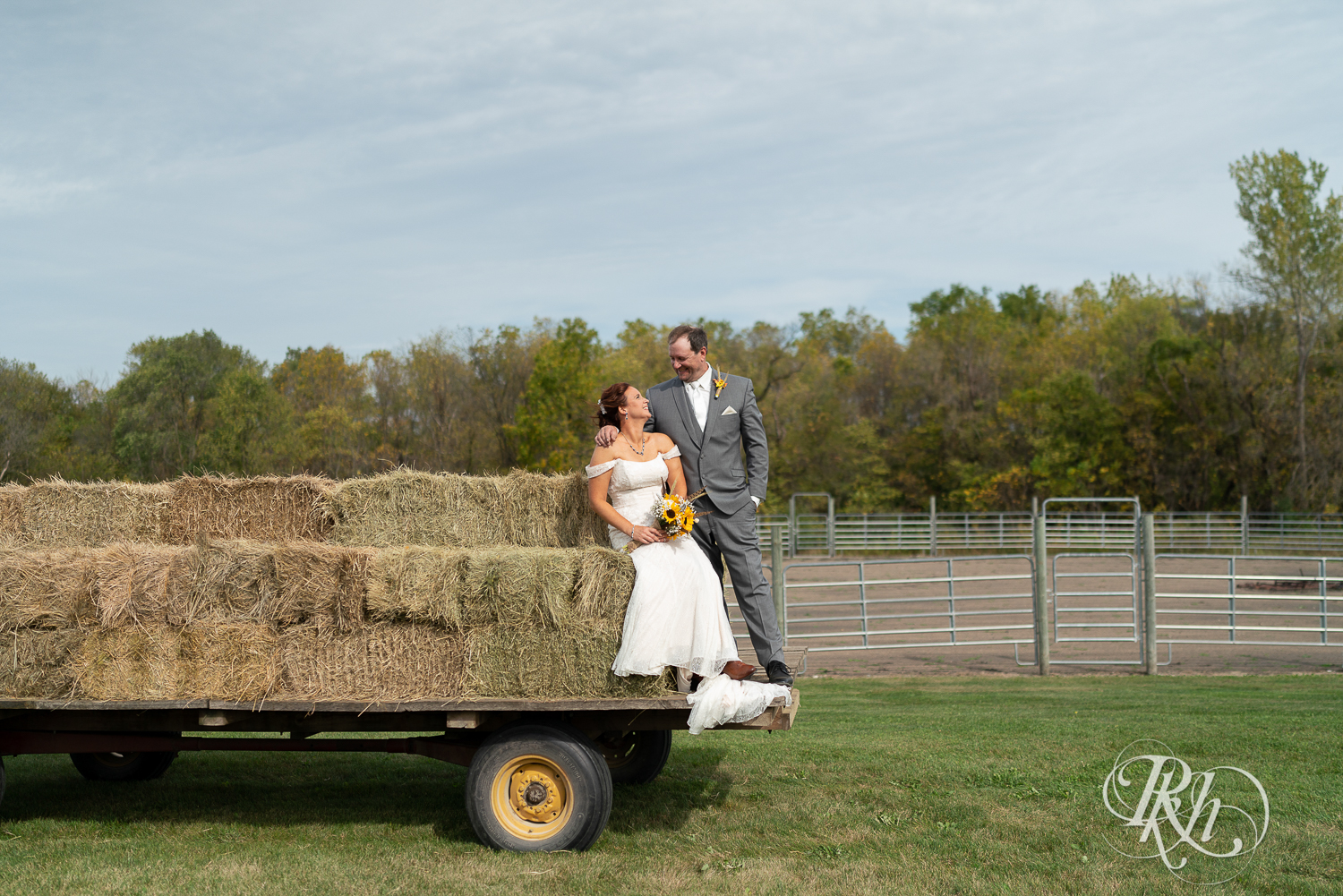 Bride and groom smiling while sitting on haystacks at Barn at Crocker's Creek in Faribault, Minnesota.