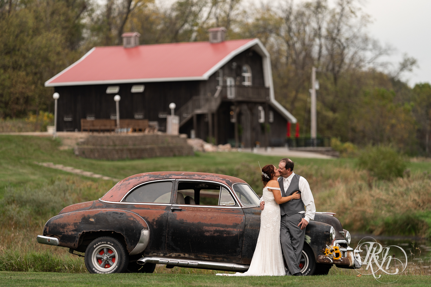 Bride and groom kissing by classic car at Barn at Crocker's Creek in Faribault, Minnesota.