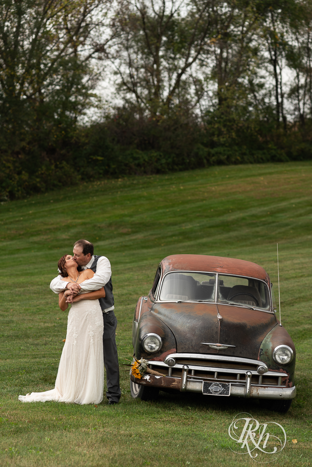 Bride and groom kissing by classic car at Barn at Crocker's Creek in Faribault, Minnesota.
