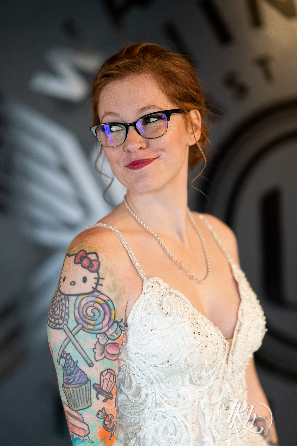 Tattooed bride with glasses smiling and looking over shoulder at Warehouse Winery in Saint Louis Park, Minnesota.