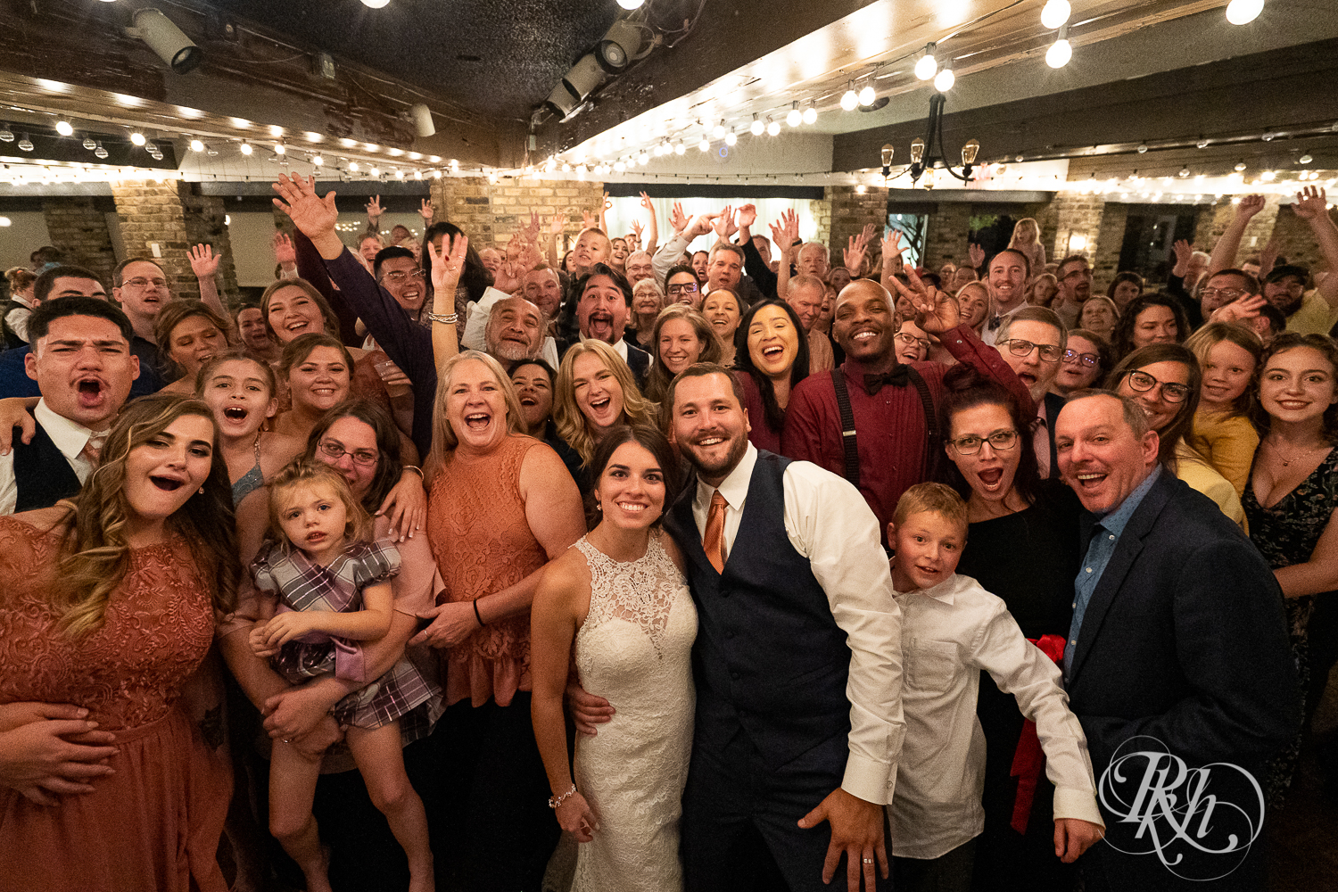 Bride and groom pose for photo with all guests during wedding reception at The Chart House in Lakeville, Minnesota.